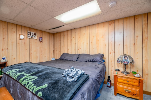 bedroom featuring wood walls, a drop ceiling, and carpet floors