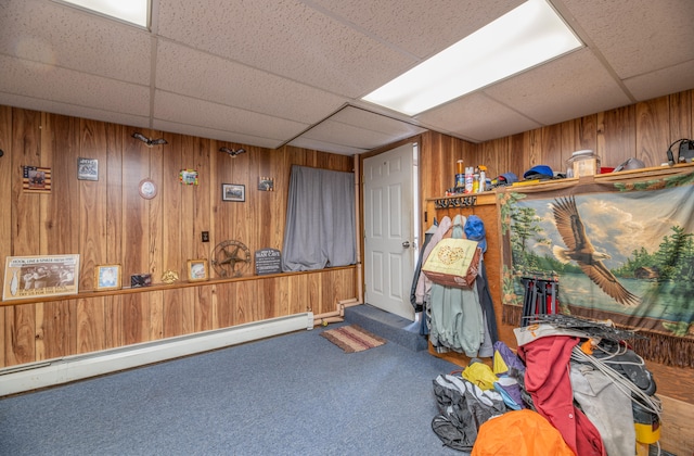misc room with a paneled ceiling, carpet flooring, wood walls, and a baseboard heating unit