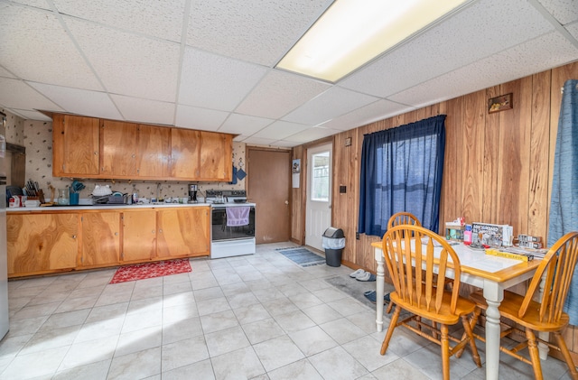 kitchen with light tile patterned floors, white stove, a paneled ceiling, and wood walls