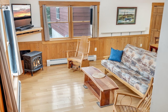 sitting room featuring light wood-type flooring, wood walls, a wood stove, and a baseboard heating unit