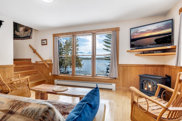 sitting room featuring wood walls, baseboard heating, a wood stove, and light hardwood / wood-style flooring