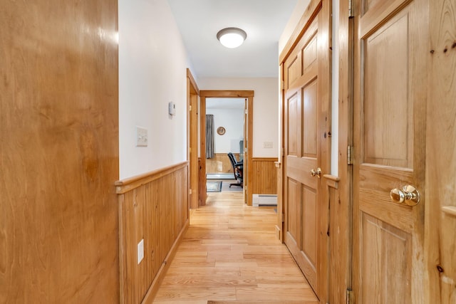 corridor with light hardwood / wood-style floors, a baseboard radiator, and wooden walls