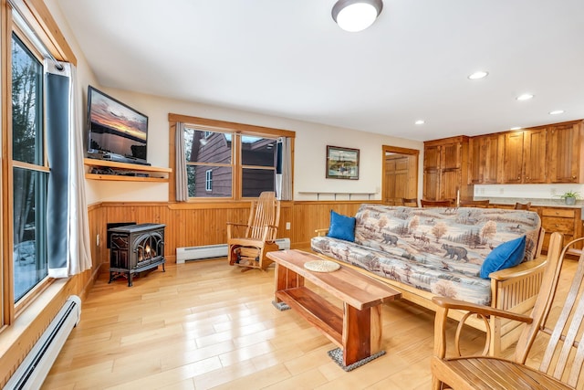 living room with baseboard heating, wood walls, a wood stove, and light hardwood / wood-style floors