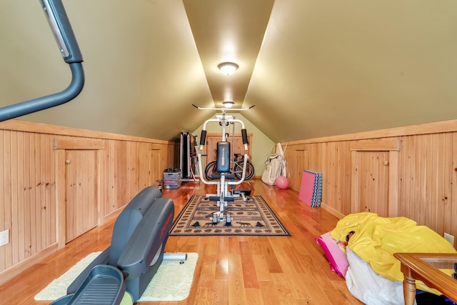 exercise area featuring light hardwood / wood-style floors, wood walls, and vaulted ceiling