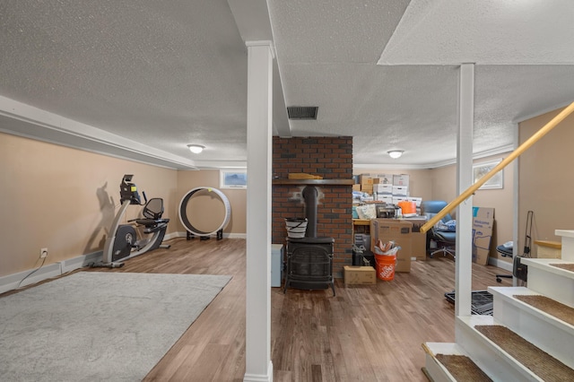 exercise room featuring a wood stove, wood-type flooring, and a textured ceiling