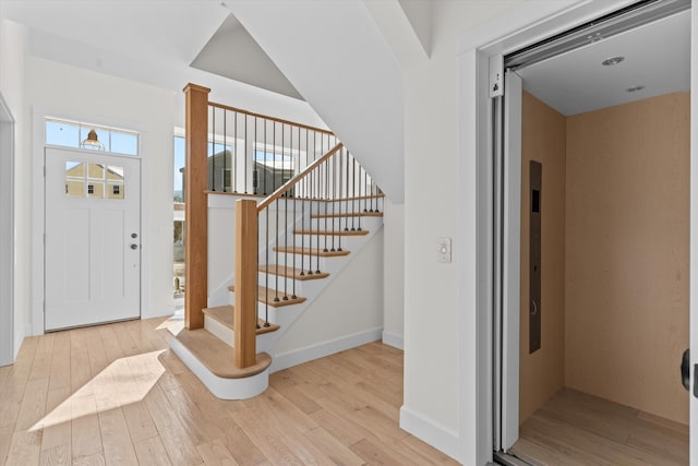 entryway featuring stairs, light wood-type flooring, baseboards, and elevator