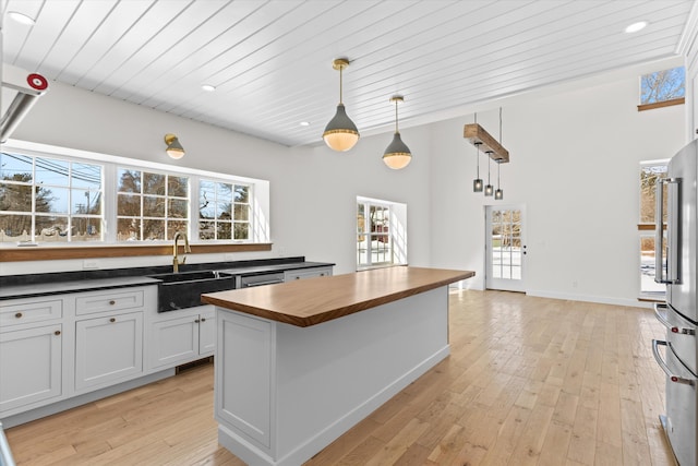 kitchen with butcher block counters, white cabinets, appliances with stainless steel finishes, a center island, and pendant lighting