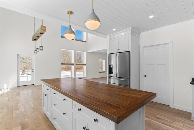 kitchen featuring high quality fridge, butcher block counters, white cabinets, a center island, and decorative light fixtures