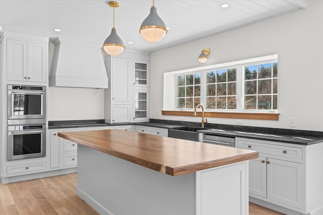 kitchen with custom exhaust hood, white cabinetry, a sink, a kitchen island, and wood counters