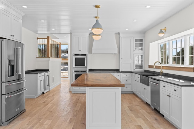 kitchen with white cabinets, glass insert cabinets, appliances with stainless steel finishes, a center island, and a sink