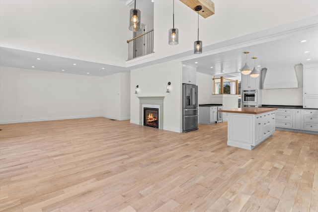 kitchen featuring high end refrigerator, open floor plan, decorative light fixtures, custom exhaust hood, and wooden counters