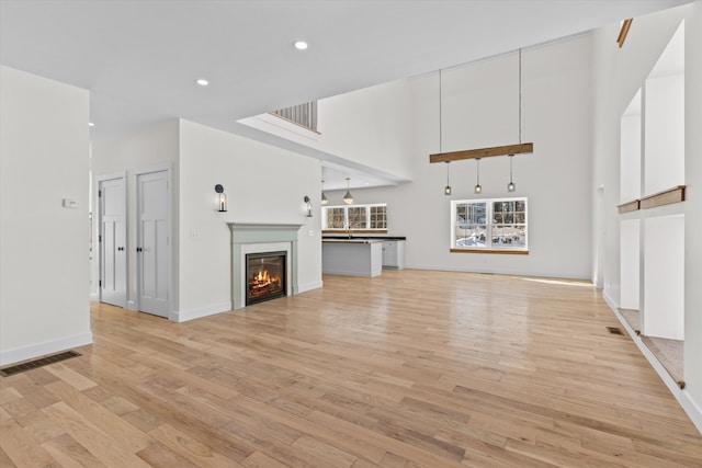 unfurnished living room with light wood-type flooring, a glass covered fireplace, visible vents, and recessed lighting