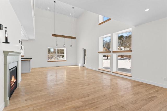 unfurnished living room featuring a towering ceiling, light wood finished floors, baseboards, and a glass covered fireplace