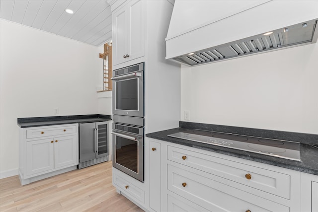 kitchen featuring white cabinets, premium range hood, black electric stovetop, and beverage cooler