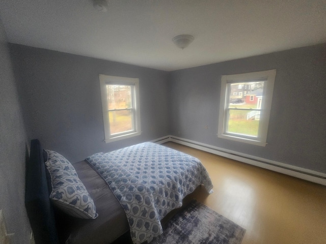 bedroom with multiple windows, hardwood / wood-style floors, and a baseboard radiator