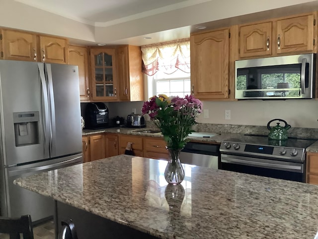 kitchen with light stone countertops, appliances with stainless steel finishes, and crown molding