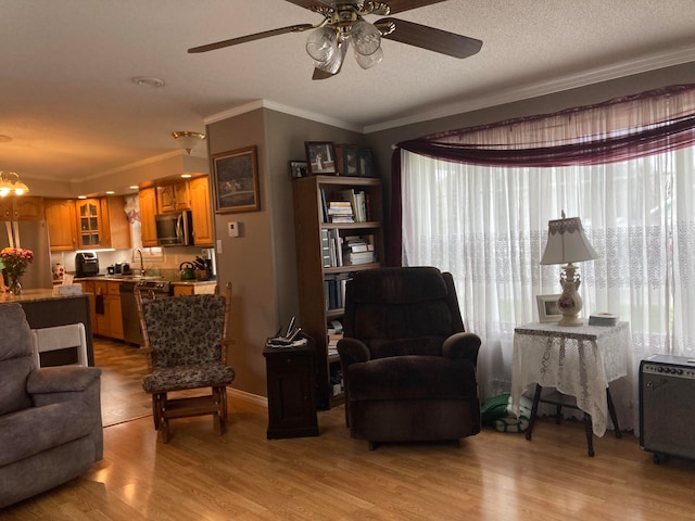 living room featuring sink, light hardwood / wood-style flooring, a textured ceiling, ceiling fan with notable chandelier, and ornamental molding