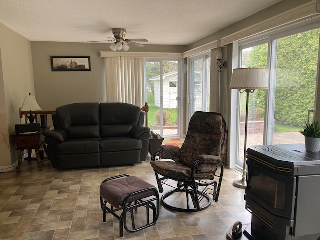 living room with a wood stove, ceiling fan, and a textured ceiling