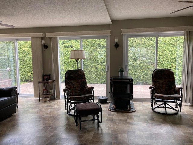 sitting room featuring ceiling fan, a healthy amount of sunlight, and a wood stove