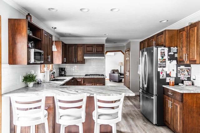 kitchen featuring a kitchen breakfast bar, hanging light fixtures, light hardwood / wood-style flooring, appliances with stainless steel finishes, and kitchen peninsula