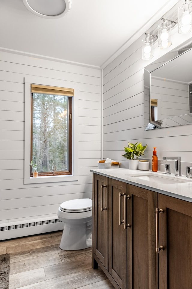 bathroom with wood-type flooring, vanity, a baseboard radiator, and wooden walls