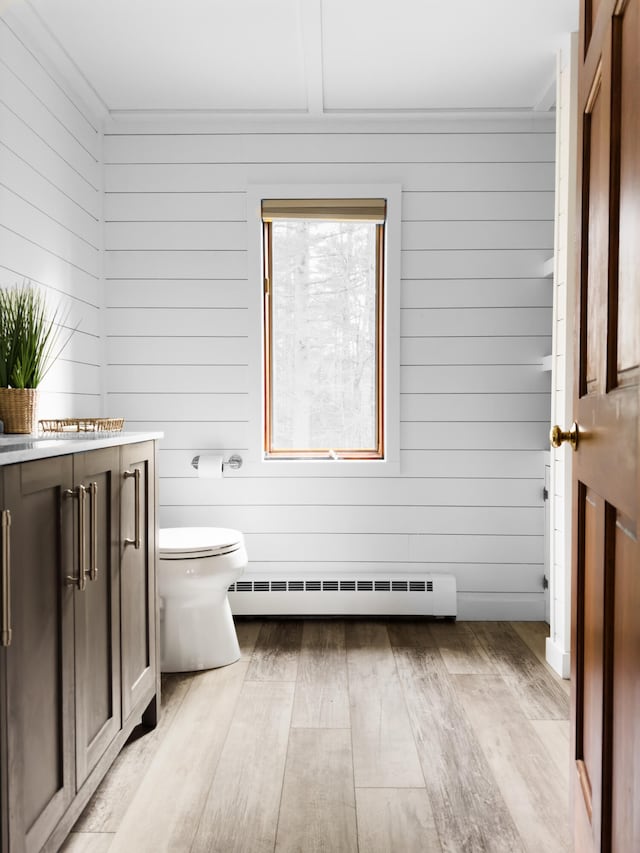 bathroom featuring baseboard heating, wood walls, hardwood / wood-style floors, crown molding, and toilet