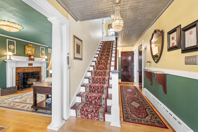 staircase featuring baseboard heating, a fireplace, wood-type flooring, and ornamental molding