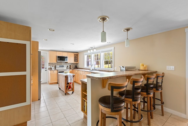 kitchen featuring kitchen peninsula, appliances with stainless steel finishes, light brown cabinetry, decorative backsplash, and a breakfast bar area