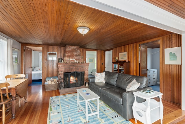 living room featuring wood walls, wood-type flooring, wood ceiling, and a brick fireplace