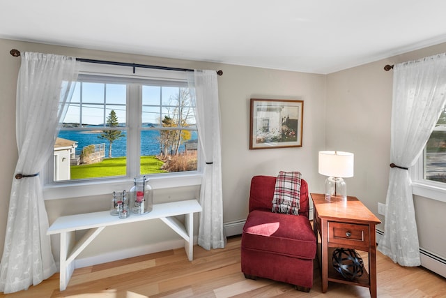living area featuring a baseboard heating unit, a water view, and light hardwood / wood-style flooring
