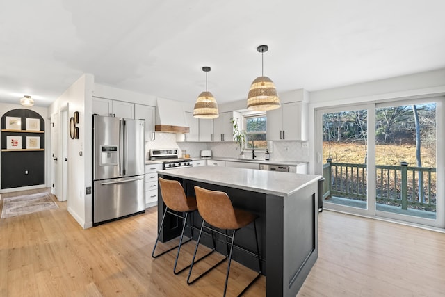 kitchen with a center island, white cabinetry, light hardwood / wood-style floors, custom range hood, and stainless steel appliances