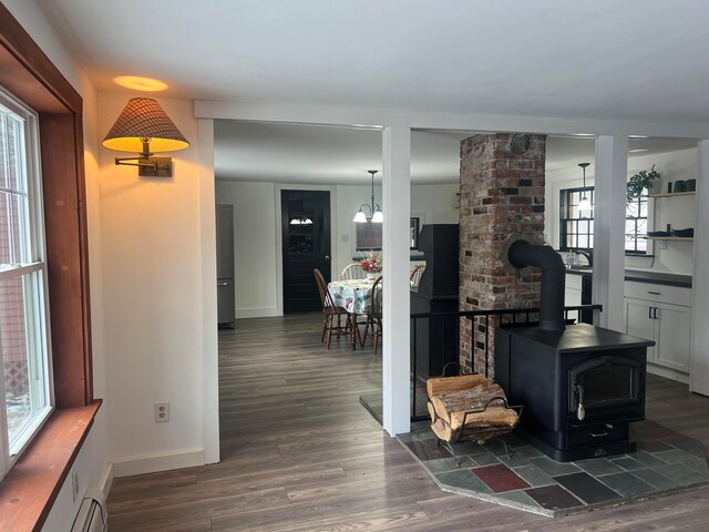 living room with a notable chandelier, plenty of natural light, dark hardwood / wood-style floors, and a wood stove