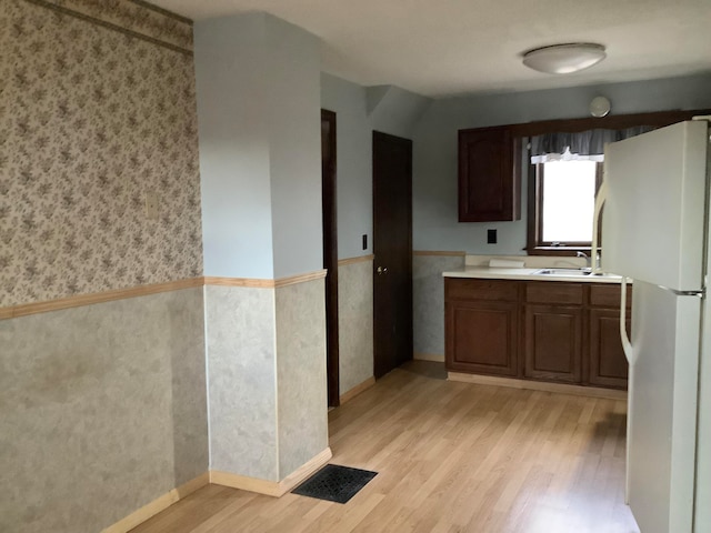 kitchen featuring dark brown cabinets, white refrigerator, light hardwood / wood-style floors, and sink