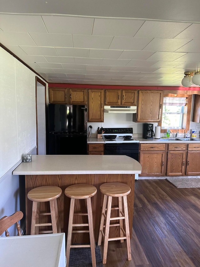 kitchen with black appliances, sink, a kitchen breakfast bar, kitchen peninsula, and dark wood-type flooring