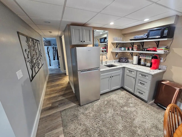 kitchen with stainless steel fridge, a drop ceiling, gray cabinetry, dark wood-type flooring, and sink