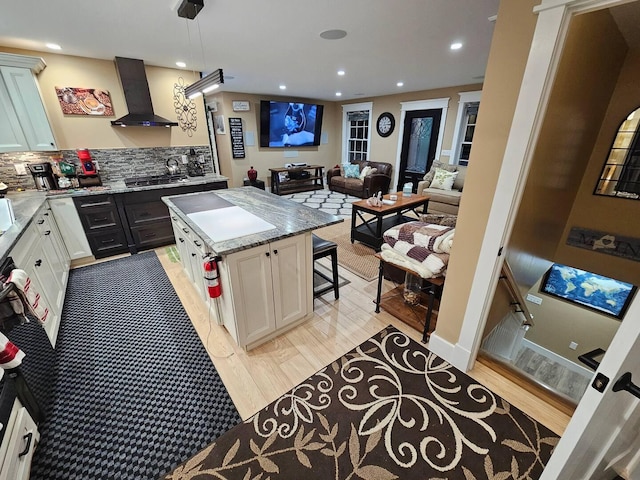 kitchen featuring a center island, wall chimney exhaust hood, pendant lighting, decorative backsplash, and light wood-type flooring