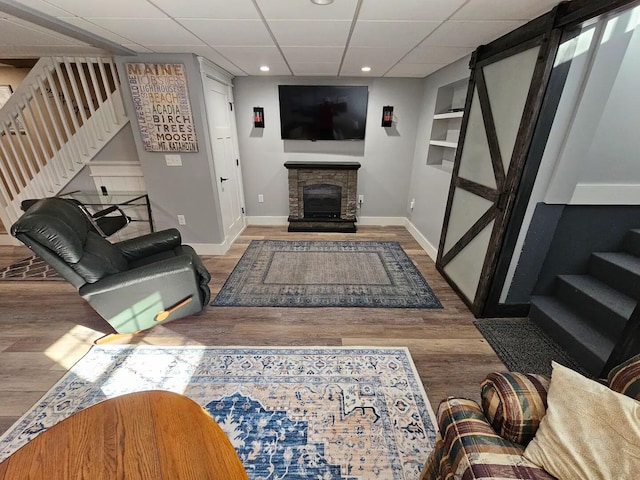 living room with a fireplace, a drop ceiling, and wood-type flooring