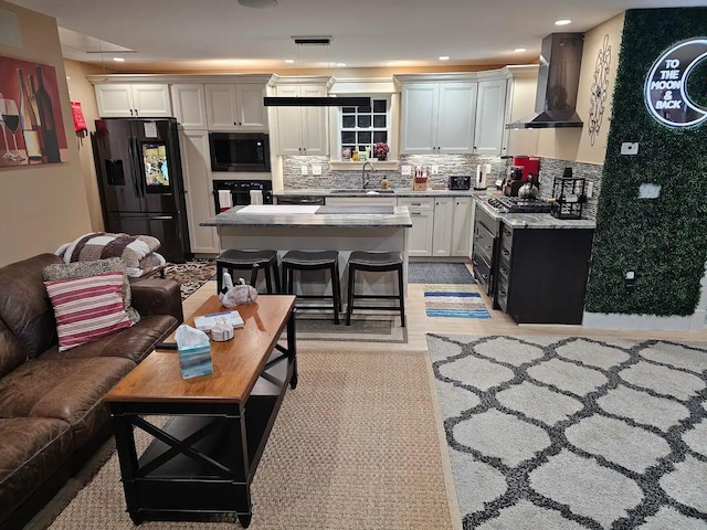 kitchen with a center island, black appliances, sink, wall chimney exhaust hood, and a kitchen bar