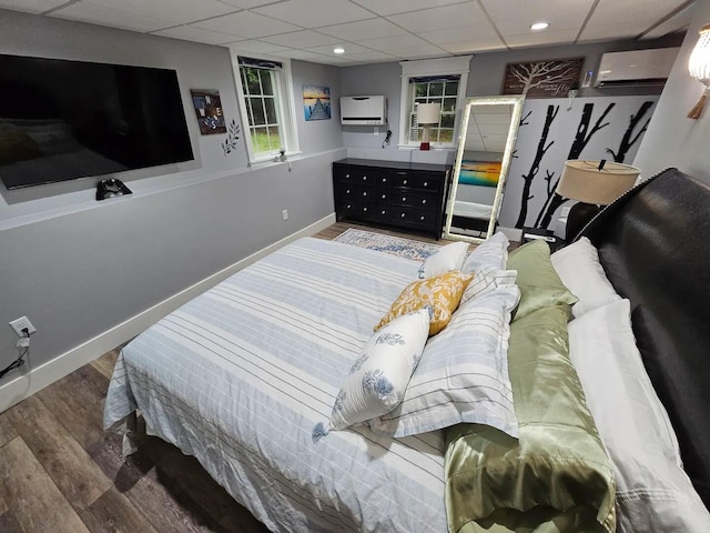 bedroom with hardwood / wood-style floors, a paneled ceiling, and an AC wall unit