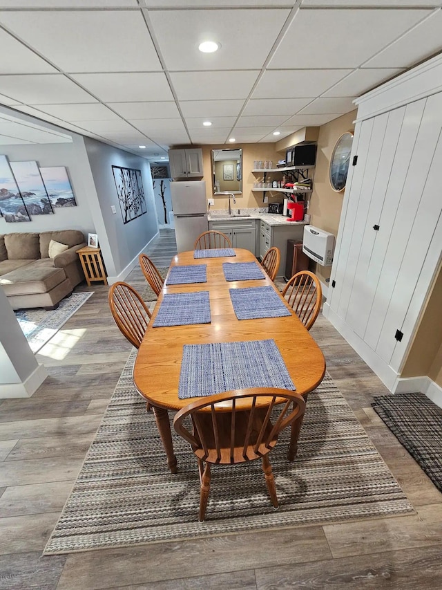 dining room with a paneled ceiling, heating unit, light hardwood / wood-style flooring, and sink