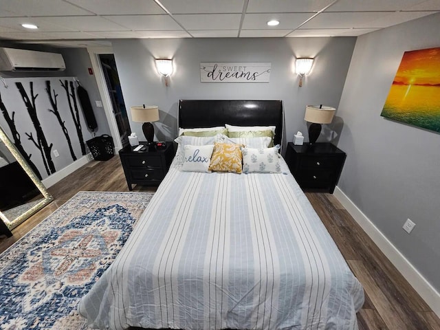 bedroom featuring dark hardwood / wood-style flooring, a wall unit AC, and a paneled ceiling