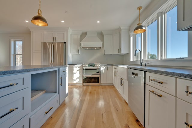 kitchen featuring white cabinets, appliances with stainless steel finishes, hanging light fixtures, and custom exhaust hood