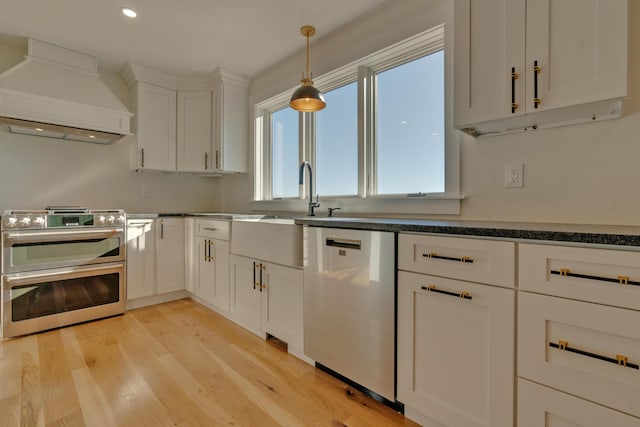 kitchen featuring white cabinets, light hardwood / wood-style floors, custom range hood, and appliances with stainless steel finishes