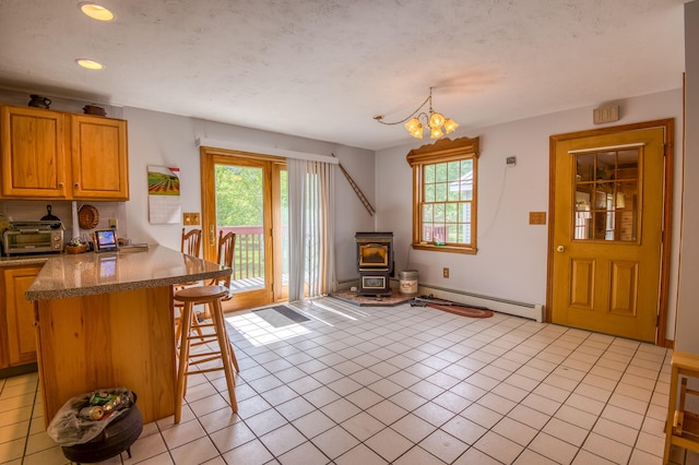 kitchen with a breakfast bar, a wood stove, a baseboard heating unit, and light tile patterned flooring