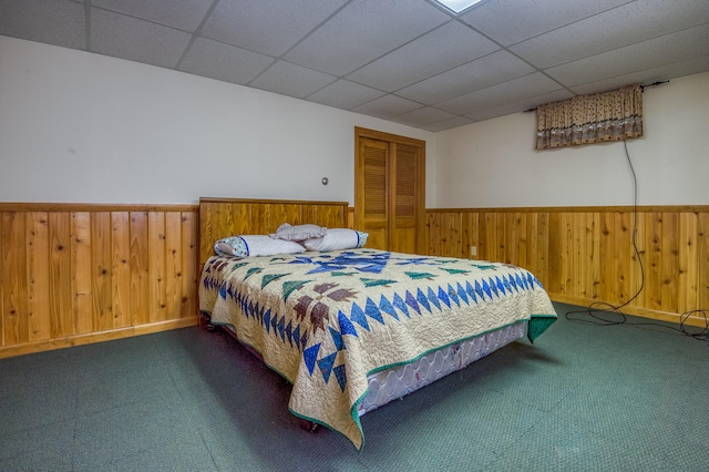 carpeted bedroom with a drop ceiling, wood walls, and a closet