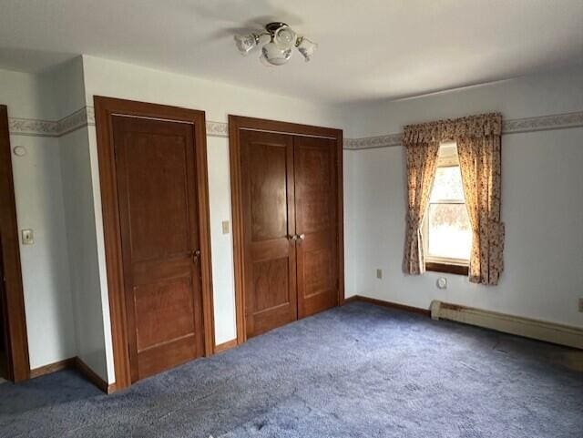 unfurnished bedroom featuring dark colored carpet, a baseboard heating unit, and multiple closets