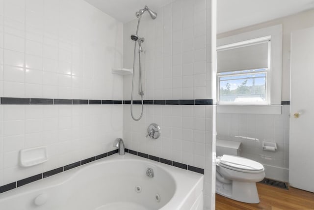 bathroom featuring hardwood / wood-style floors, tiled shower / bath, tile walls, and toilet