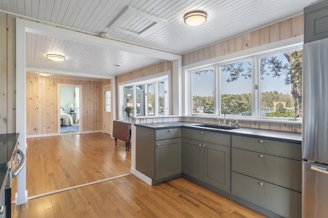 kitchen featuring gray cabinetry, sink, stainless steel fridge, wooden walls, and light wood-type flooring