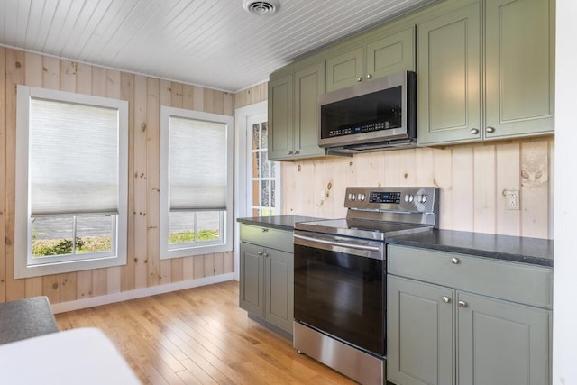 kitchen featuring appliances with stainless steel finishes, light hardwood / wood-style flooring, green cabinets, and wood walls