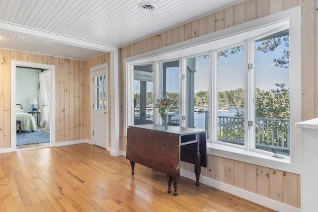 interior space featuring light hardwood / wood-style floors, wood ceiling, a water view, and wood walls